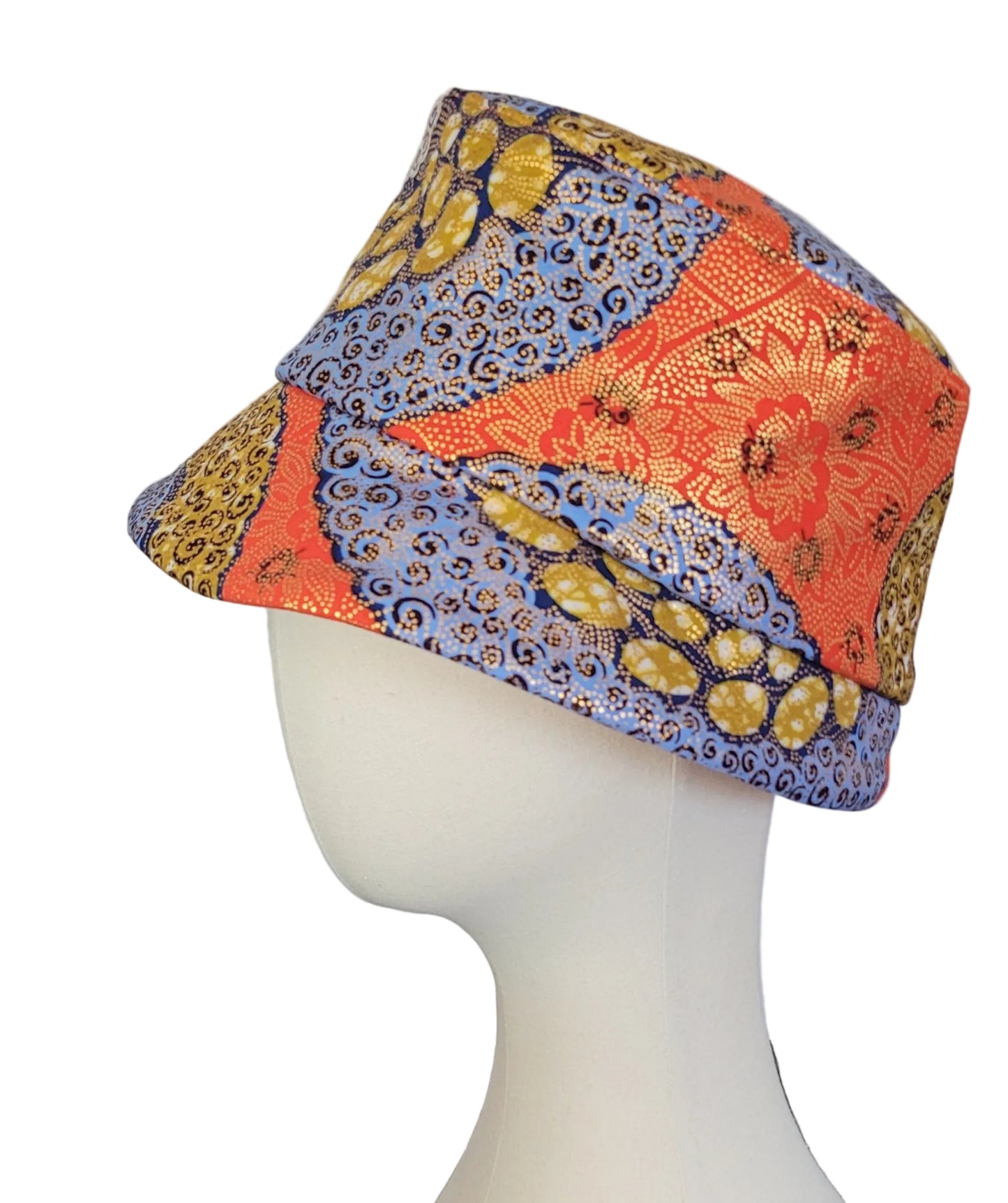 A multicolor patterned bucket hat displayed on a white mannequin head. The hat features a patchwork design with orange floral brocade, blue paisley, and yellow-gold leopard print panels.