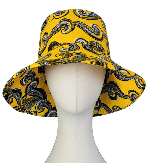 A wide-brimmed bucket hat with a vibrant yellow base and a black, white, and dark blue swirling wave pattern, displayed on a white mannequin.