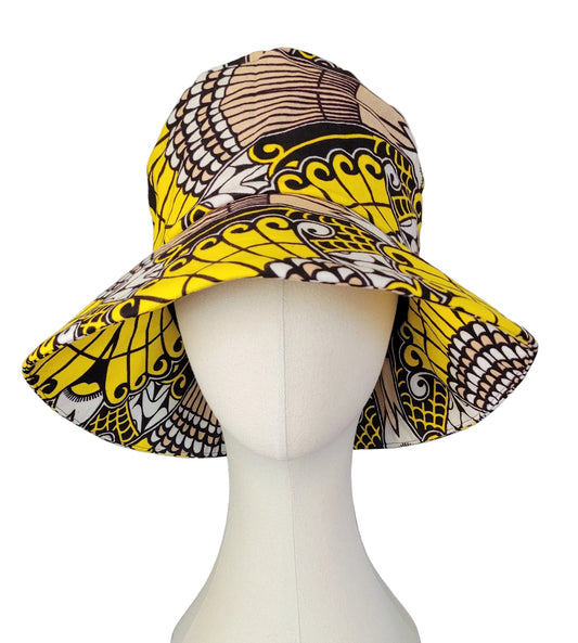 A wide-brim sun hat with a bold yellow, black, and brown African wax print pattern, displayed on a white mannequin head.